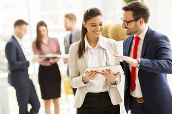 Young business couple is working on a tablet while other young business people talking in the background